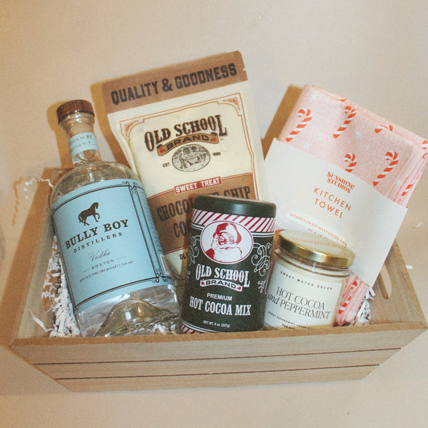 Example of holiday gift basket with hot cocoa, cookie mix, vodka, a tea towel and candle